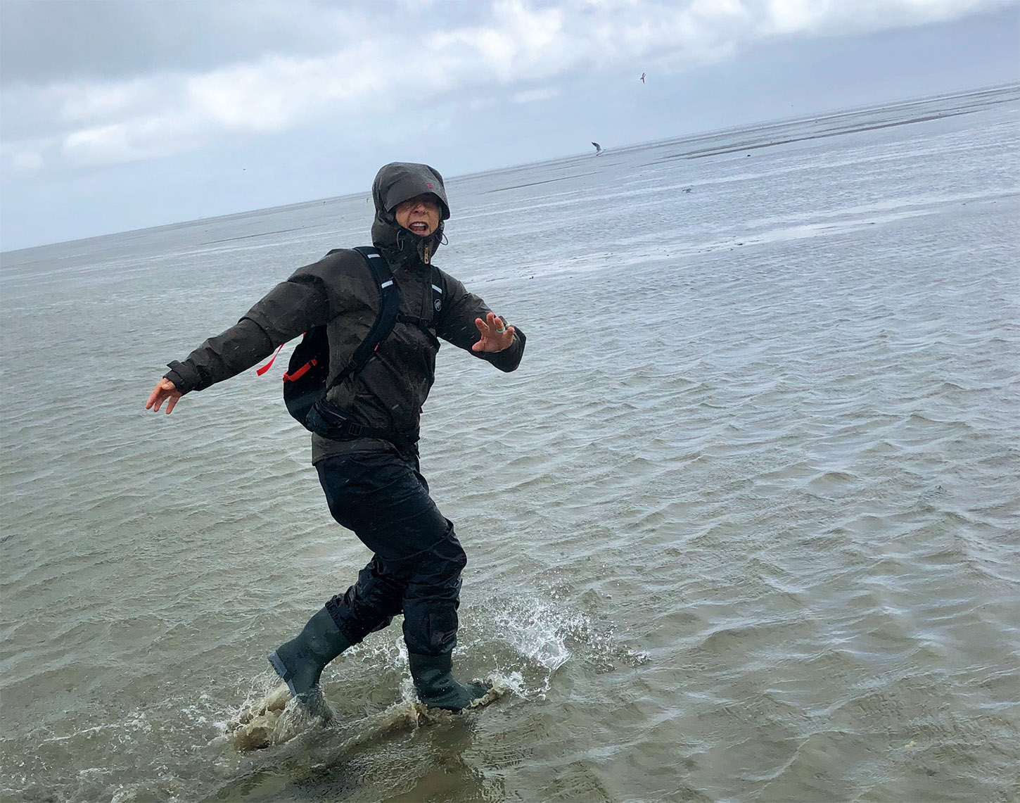 vrouw in regenpak tot haar enkels in de zee