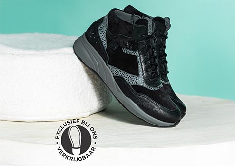 een paar halfhoge sneakers donker tegen kussen