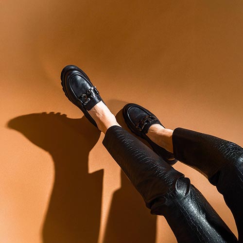 2 damesbenen met zwart leren broek en zwarte loafers